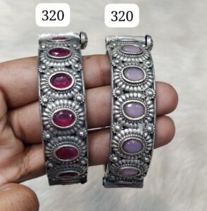 Two silver bangles adorned with pink and red stones, showcasing intricate designs and craftsmanship.