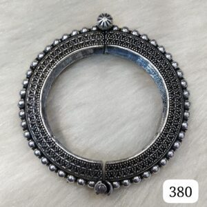 A circular silver decorative bangle with intricate detailing and a small clasp mechanism.