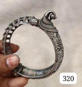 Silver bangle with intricate patterns and a decorative peacock design on top.