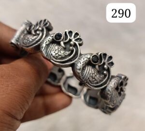 Intricately designed silver bracelet featuring peacock motifs and black stones, held in a hand.
