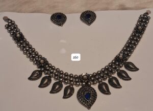 Traditional silver necklace with blue stones and matching earrings displayed on a white background.