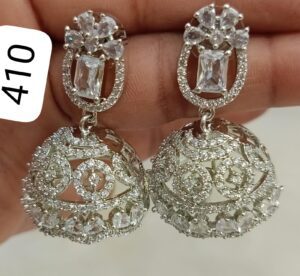 A pair of silver earrings featuring intricate designs and clear crystals, held in a hand.