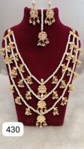 Traditional gold and pearl necklace set displayed on a red velvet bust with matching earrings.