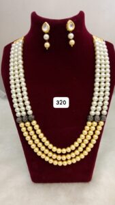 Three-layered pearl necklace in white and gold with matching earrings displayed on a bust.