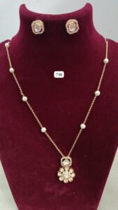 Gold necklace with pearl accents and matching earrings displayed on a maroon velvet stand.