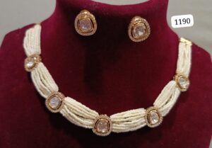 Gold and pearl beaded necklace with matching earrings displayed on a maroon background.