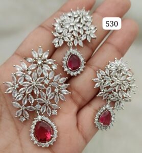 Hand holding a silver jewelry set featuring red gemstones and intricate designs.