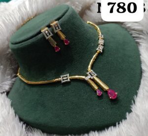 Gold necklace and earrings set with ruby accents and diamond-like embellishments displayed on a green velvet stand.