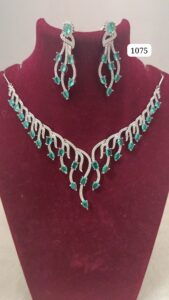 Emerald and silver necklace with matching earrings displayed on a red velvet bust.