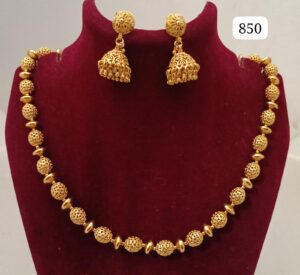 Gold necklace with intricate bead designs and matching earrings displayed on a velvet stand.