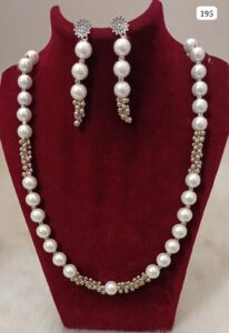 A pearl necklace with decorative elements and matching earrings displayed on a velvet bust.