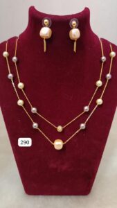 Gold necklace with pearls and matching earrings displayed on a velvet bust.