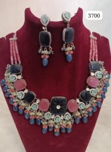 Multicolored necklace with large stones and matching earrings displayed on a velvet bust.