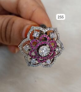 Floral pendant with pink stones and clear crystals held by a hand.