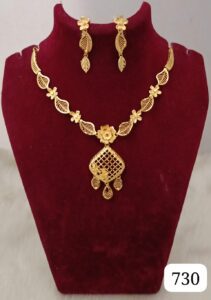 Gold necklace with floral and leaf designs, accompanied by matching earrings displayed on a velvet stand.