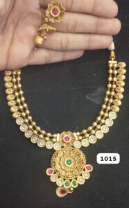 Gold necklace with intricate design and colorful stones held in a hand.