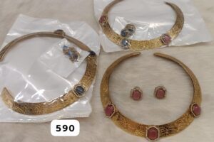 Three gold necklaces with intricate designs and colored stones, along with matching earrings in clear packaging.